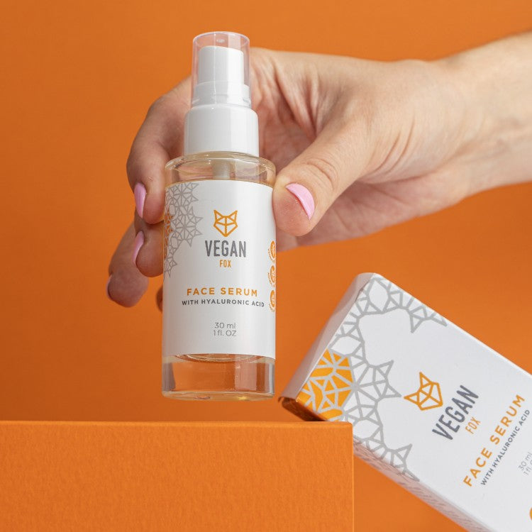 Vegan Fox Hyaluronic Acid Face Serum bottle with pump and matching box held in hand on orange background