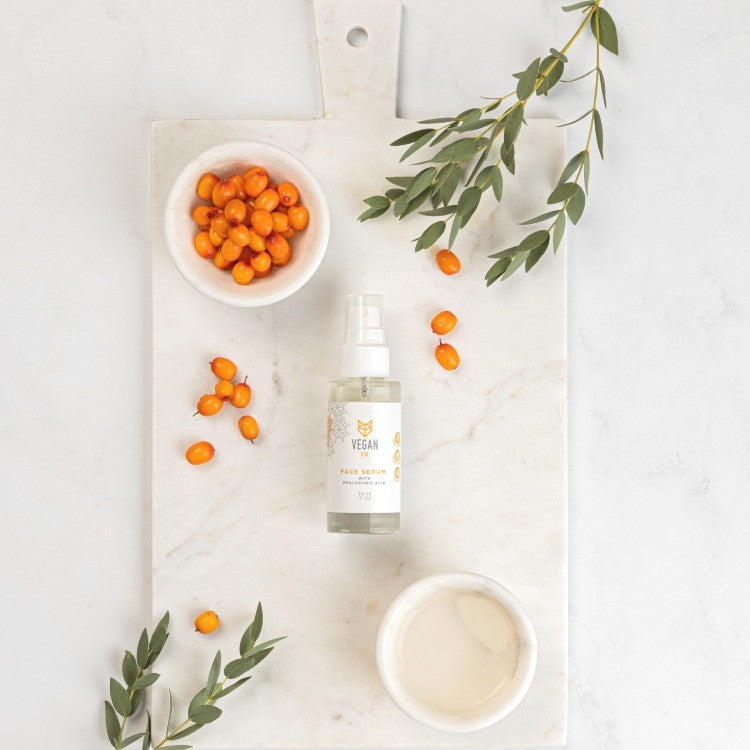 Vegan Fox Hyaluronic Acid Face Serum bottle on marble board with sea buckthorn berries and green leaves