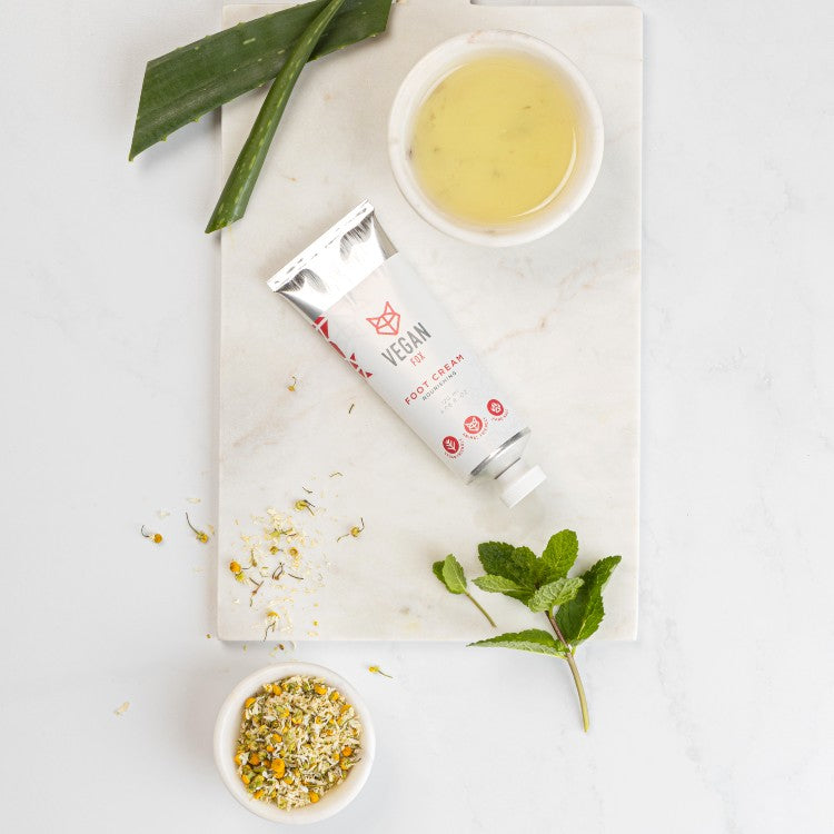 Vegan Fox hydrating foot cream 120ml tube displayed with natural ingredients like aloe, chamomile, and mint on marble surface